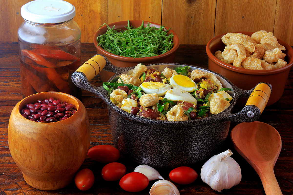 Feijao Tropeiro typical dish of Brazilian cuisine, made with beans, bacon, sausage, collard greens, eggs, on rustic wooden table. Top view